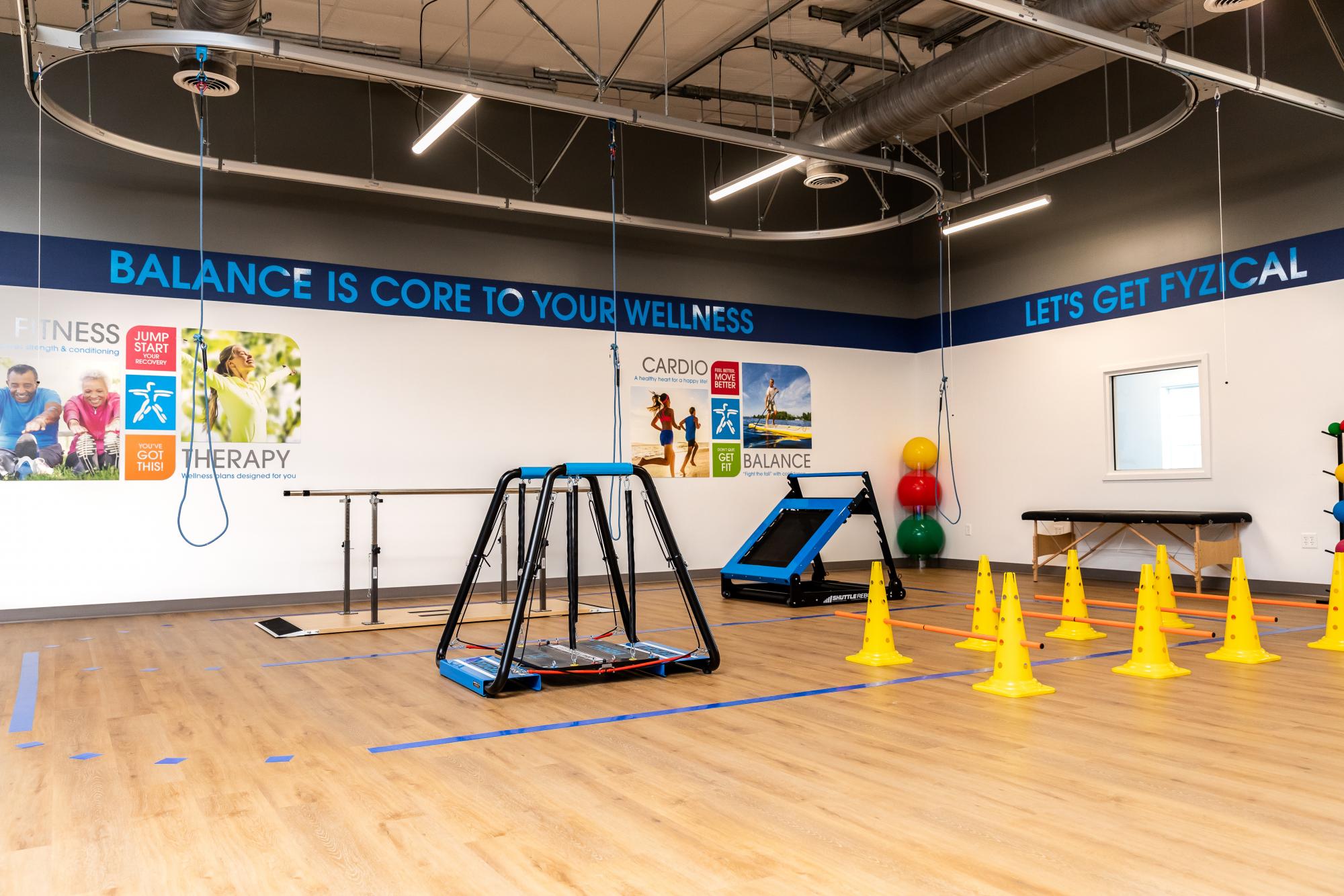 FYZICAL Therapy and Balance Centers in Douglas, GA featuring a modern balance training room with therapy equipment, obstacle cones, and body-weight support systems for physical rehabilitation and fall prevention.