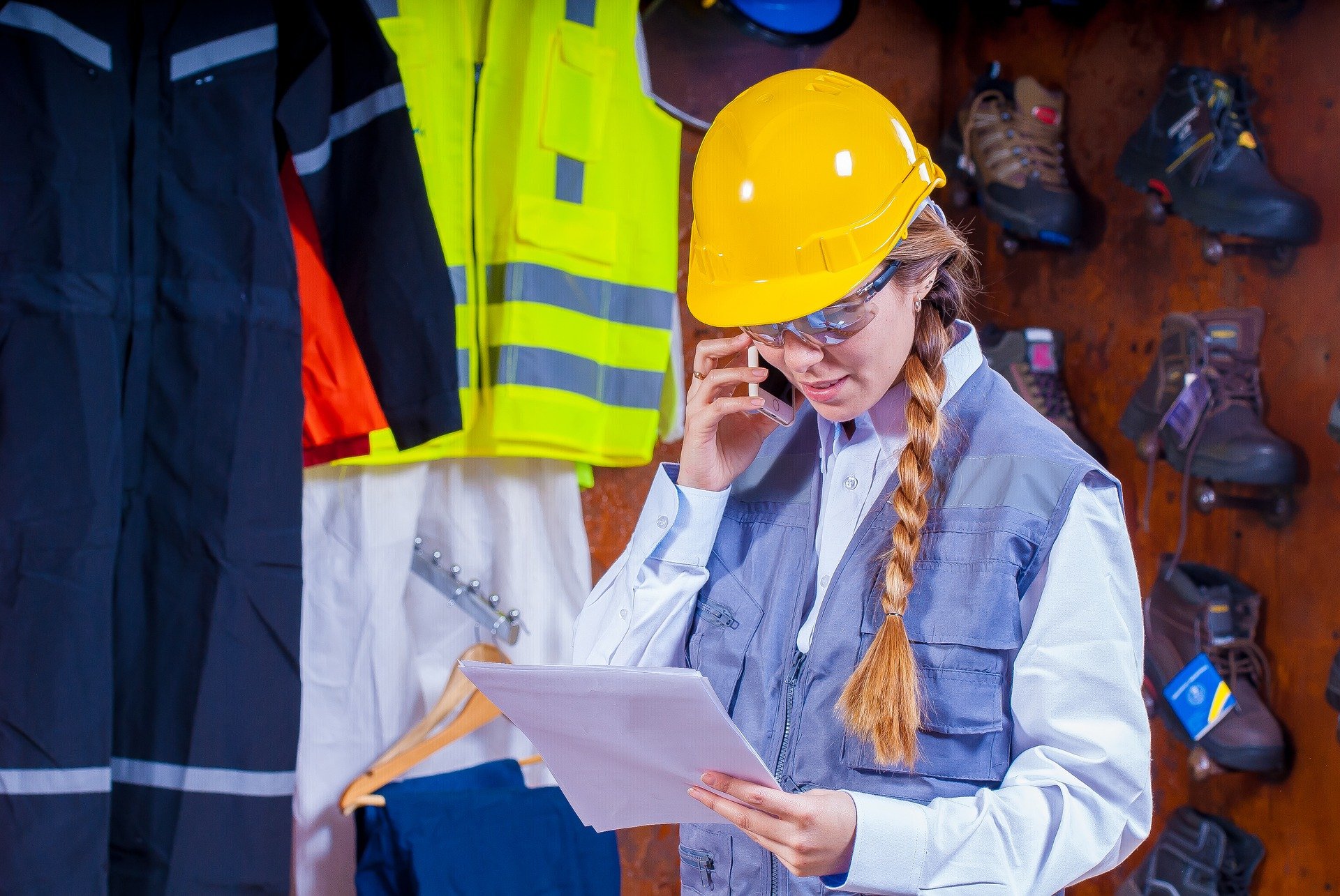 Woman wearing a hard hat and reading a document while talking on the phone