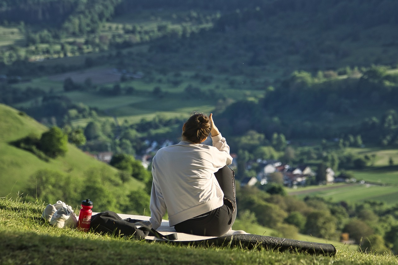 Photograph of a woman sitting on a blanket on a grassy hill, overlooking a picturesque village. This serene setting symbolizes the peaceful relief and quality of life regained after effective treatment for tailbone pain through pelvic floor physical therapy at FYZICAL Oklahoma City.